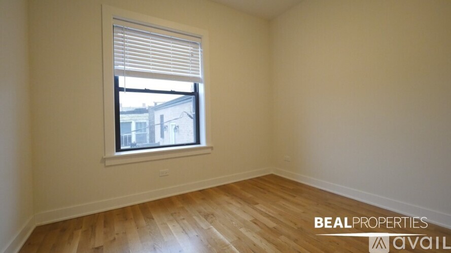 A room with wooden flooring and a window showing a view of buildings outside.