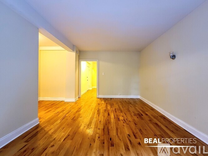 A room with wooden flooring and white walls, with a doorway leading to another room.
