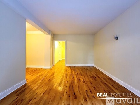A room with wooden flooring and white walls, with a doorway leading to another room.