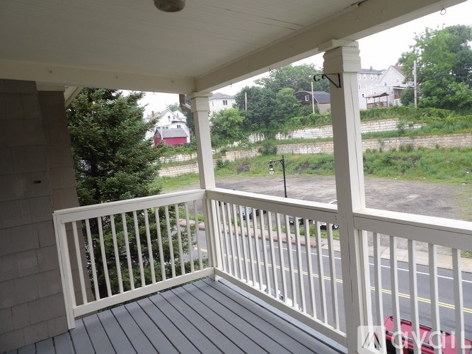 A porch with a white railing and a view of a street and houses.
