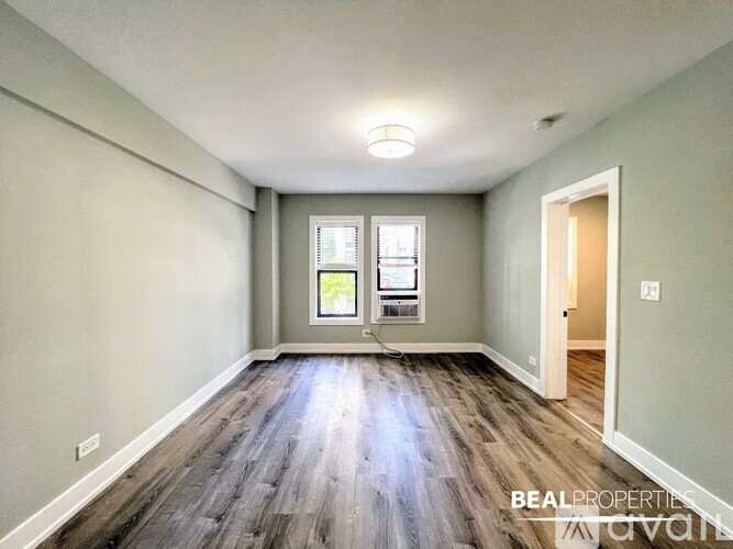A spacious room with wooden flooring and a window overlooking a tree-filled yard.