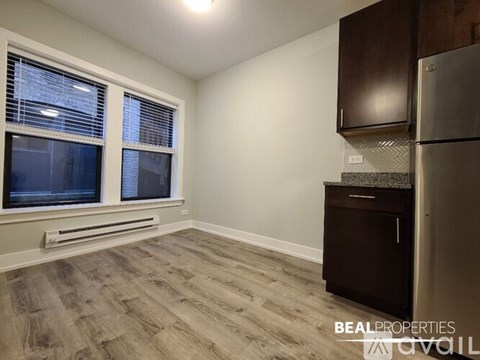 A kitchen with a refrigerator, cabinets, and a window with blinds.