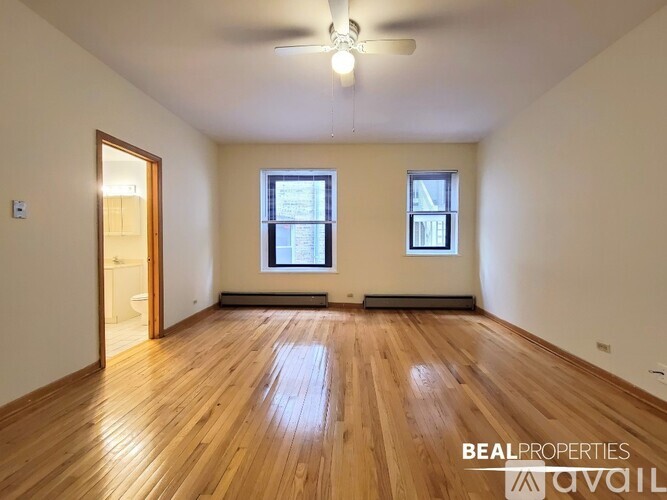 A spacious room with wooden floors and two windows.