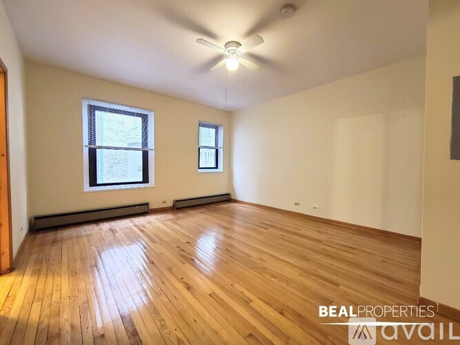 A room with wooden flooring and two windows.