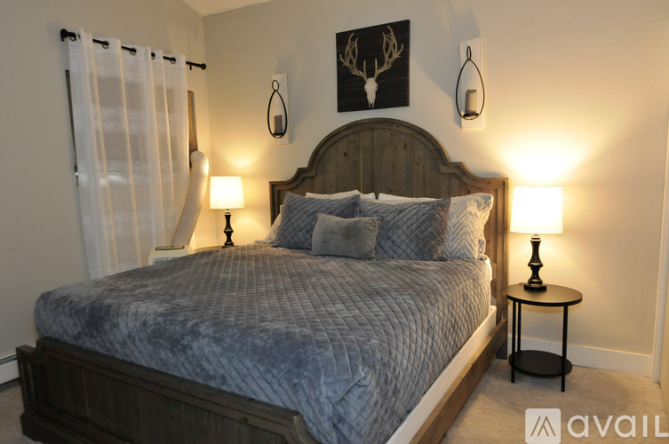 A bedroom with a bed, two lamps, and a deer head on the wall.