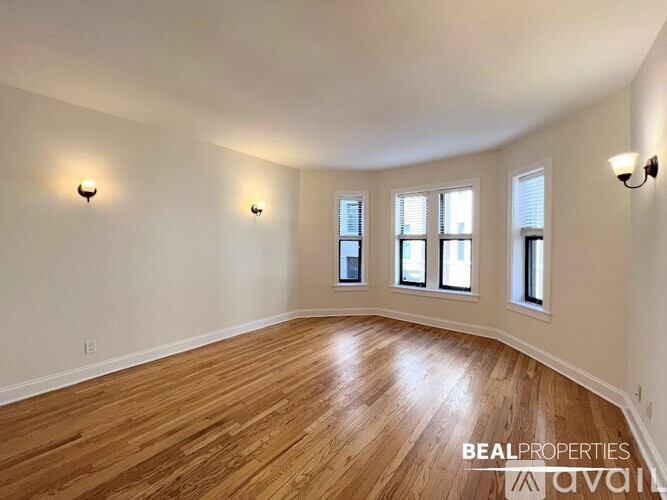 A spacious room with wooden floors and three windows.