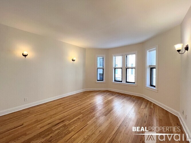 A spacious room with wooden floors and three windows.