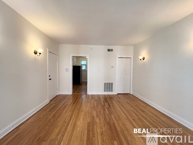 A room with wooden floors and white walls, with a door at the end of the hallway.