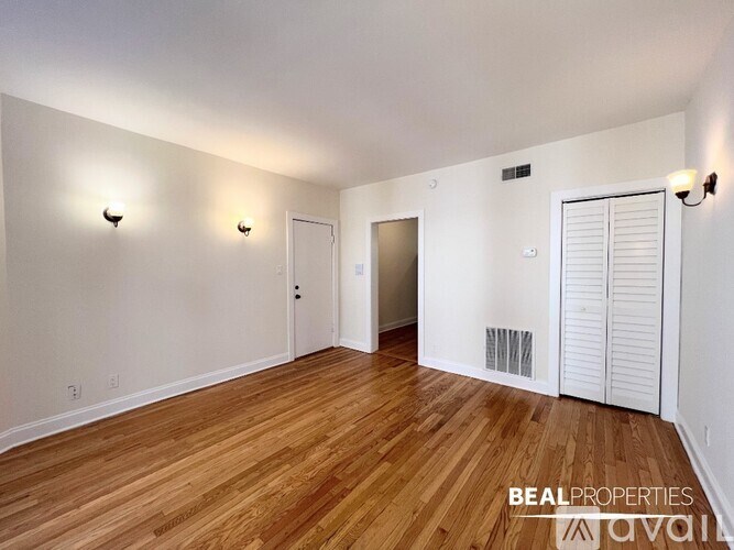A room with wooden flooring and white walls, with a door on the right and a window on the left.