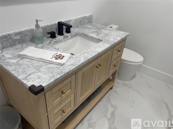A bathroom with a marble countertop and wooden cabinets.