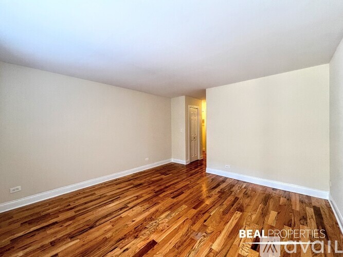 A room with wooden flooring and white walls, with a door in the background.