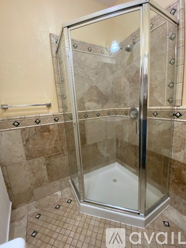 A shower with a glass door and tiled floor.