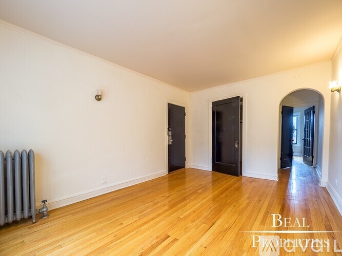 A room with wooden floors and a radiator on the left side.