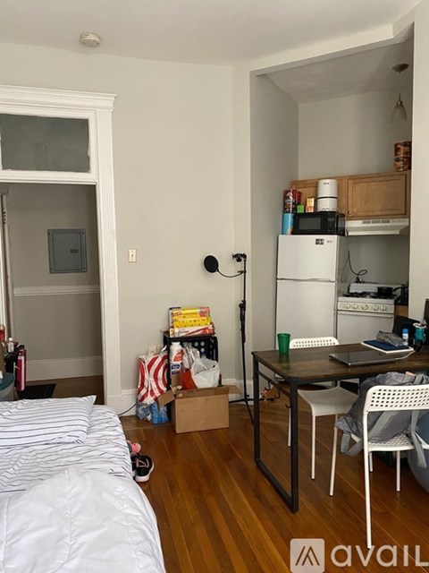 A small room with a bed, desk, and a refrigerator in the kitchen area.
