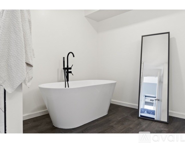 A white bathtub with a black faucet is in a bathroom with a white towel hanging on the wall.
