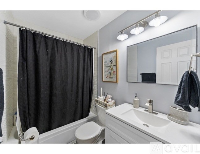 A bathroom with a white sink, toilet, and a black shower curtain.