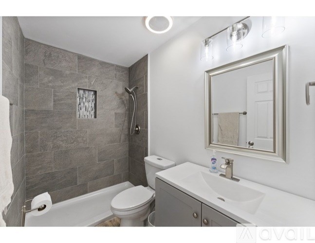 A bathroom with a white sink, toilet, and a grey tiled shower.