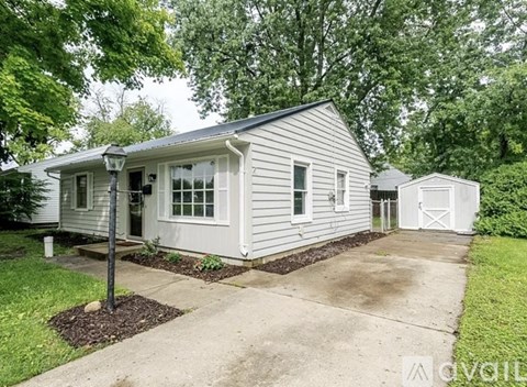A house with a grey siding and white trim is surrounded by greenery.