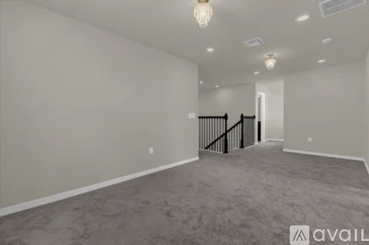 A spacious room with a carpeted floor and a staircase with a black railing.