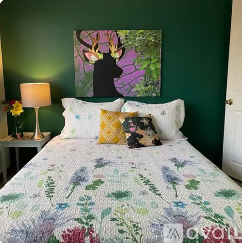A bed with a floral comforter and a painting of a deer head on the wall.