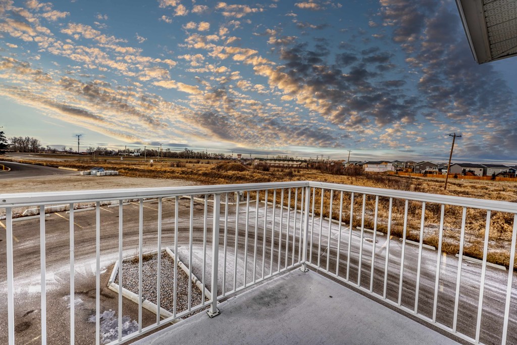 A balcony with a metal railing overlooks a parking lot.