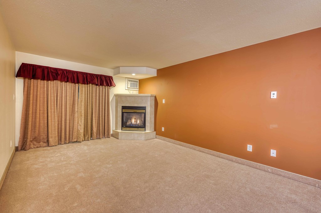 A living room with a fireplace and a window with curtains.