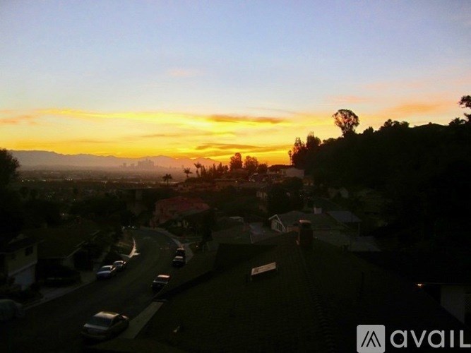 A sunset view from a high vantage point overlooking a street with cars and houses.