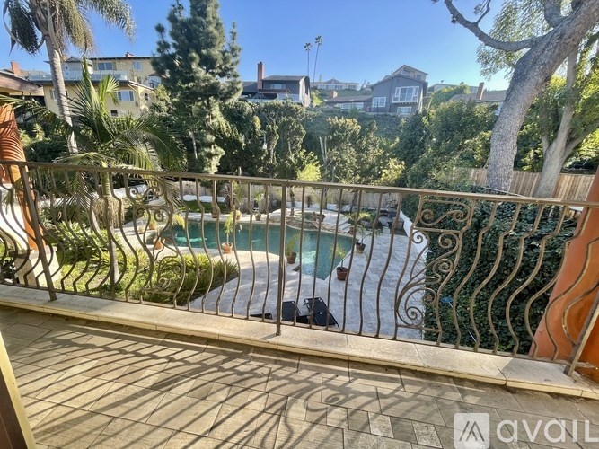 A balcony with a metal railing overlooks a pool and a residential area.