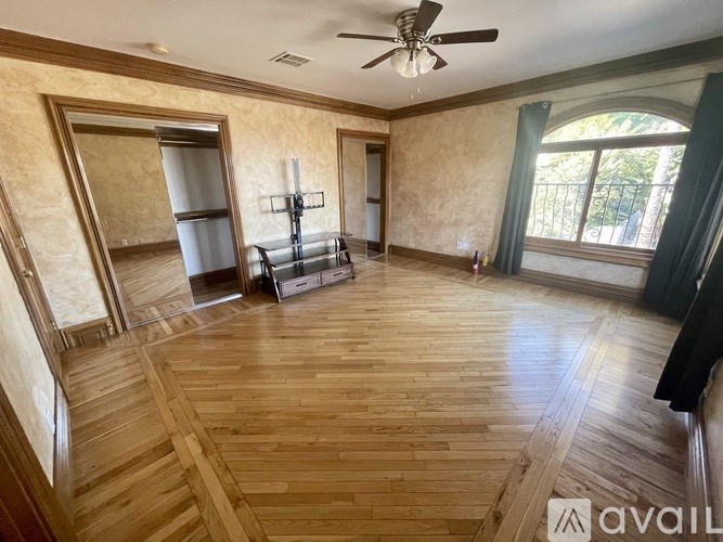 A spacious room with wooden flooring and a ceiling fan.
