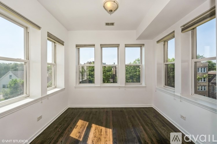 A room with wooden floors and white walls, featuring a large window with a view of trees and a house.
