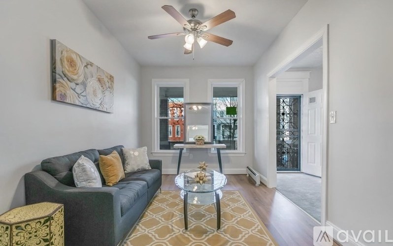 A living room with a grey couch, a glass coffee table, and a painting on the wall.