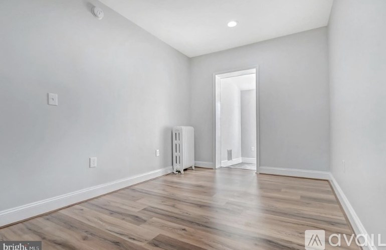 A spacious room with wooden flooring and a white wall.