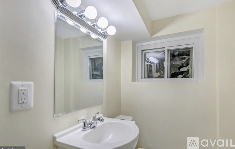 A bathroom with a white sink and a mirror with lights above it.