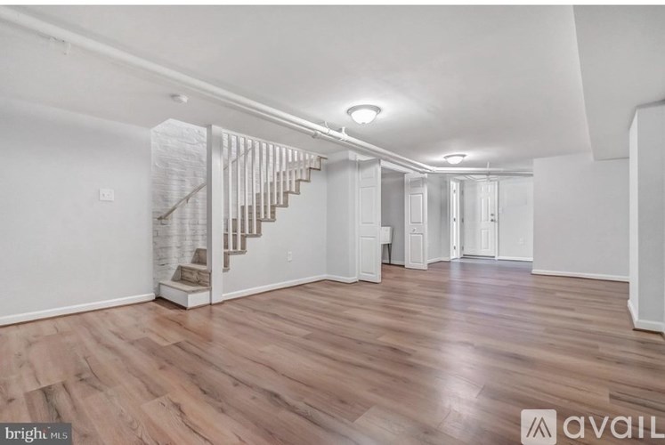 A spacious room with wooden flooring and a staircase with a glass railing.