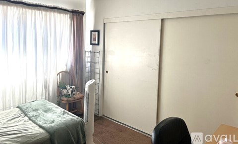 A bedroom with a bed, chair, and a window with curtains.