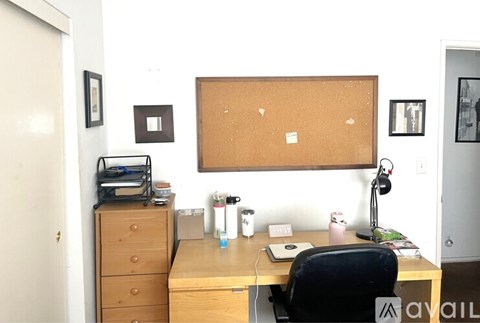 A small office with a wooden desk and a cork board on the wall.