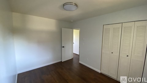 A room with white walls and wooden floors, with a white door and a white cabinet with a light switch on the wall.