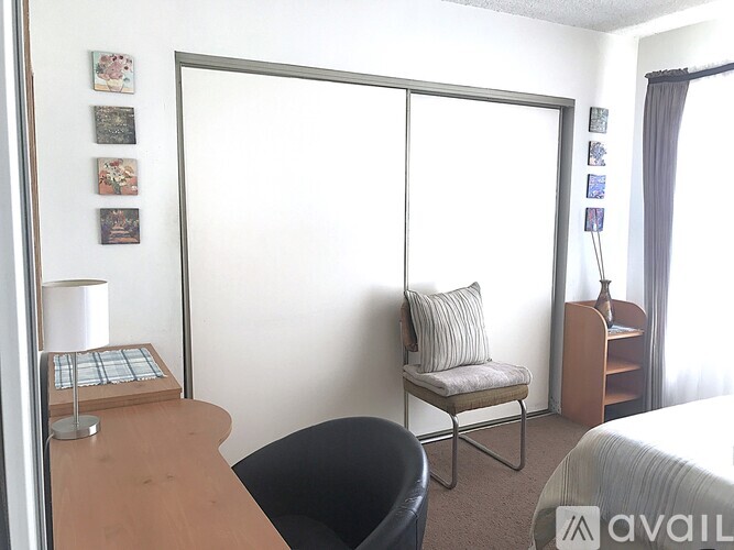 A room with a bed, a chair, a desk, and a table with a lamp on it.