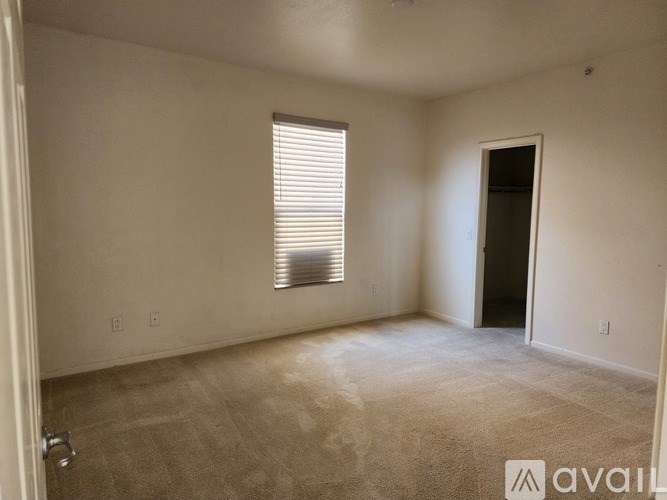 A room with a carpeted floor, a window with blinds, and a door leading to another room.