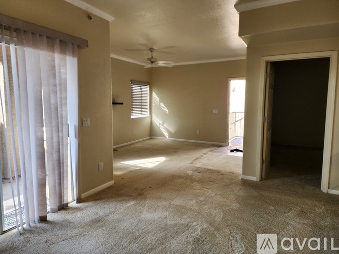 A spacious room with a carpeted floor, a ceiling fan, and a door leading to another room.
