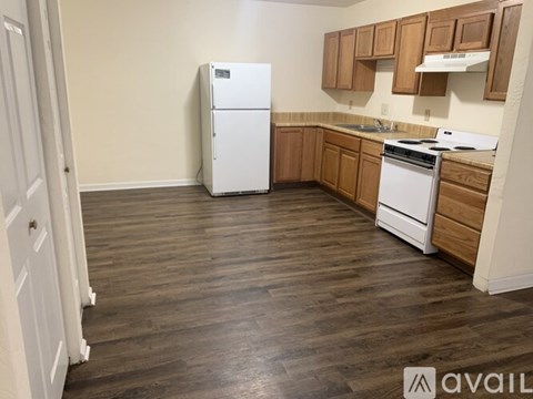 A kitchen with a white refrigerator and stove, wooden cabinets, and a wooden floor.
