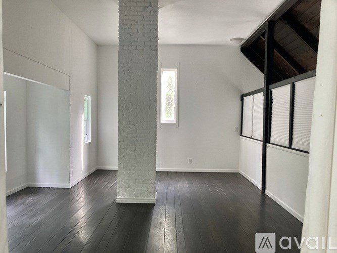 A room with a white column and wooden floors is available for rent.