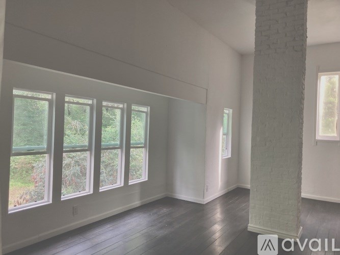 A room with white walls and a large window with a view of greenery outside.