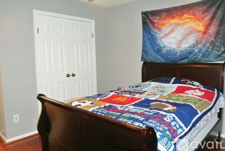 A bedroom with a bed covered in a baseball-themed comforter.
