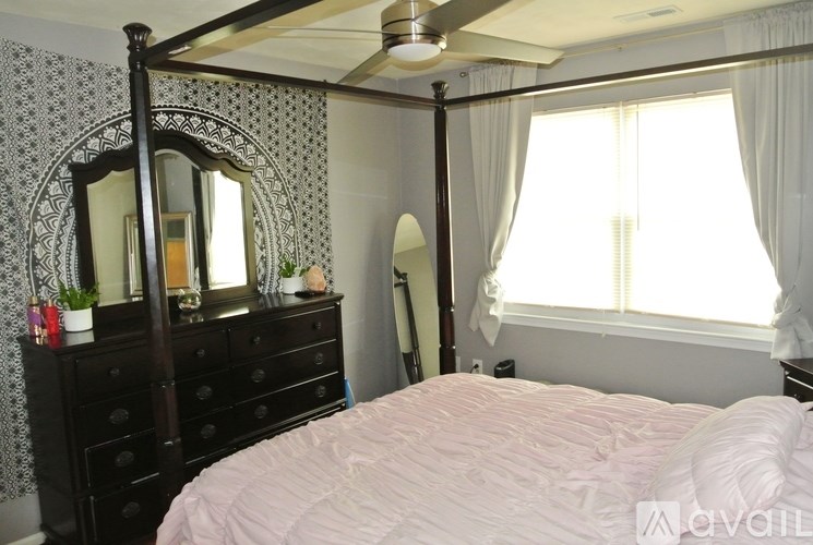 A bedroom with a large bed, a dresser with a mirror, and a window with curtains.