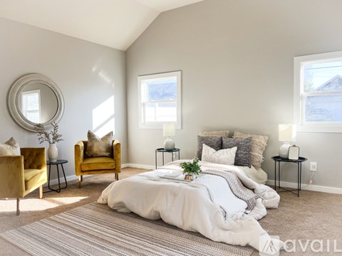 A bedroom with a large bed, a yellow chair, and a round mirror on the wall.