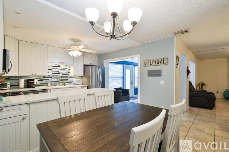 A kitchen with a wooden table and chairs in the foreground and a living room in the background.