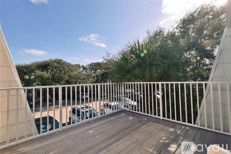 A balcony with a white railing and a view of a parking lot and trees.