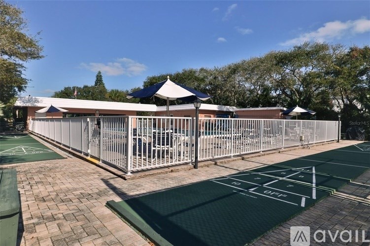 A tennis court with a green surface and white lines, surrounded by a metal fence and a building in the background.