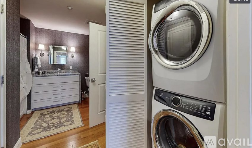 A washing machine is in the foreground of a bathroom with a mirror and a cabinet.